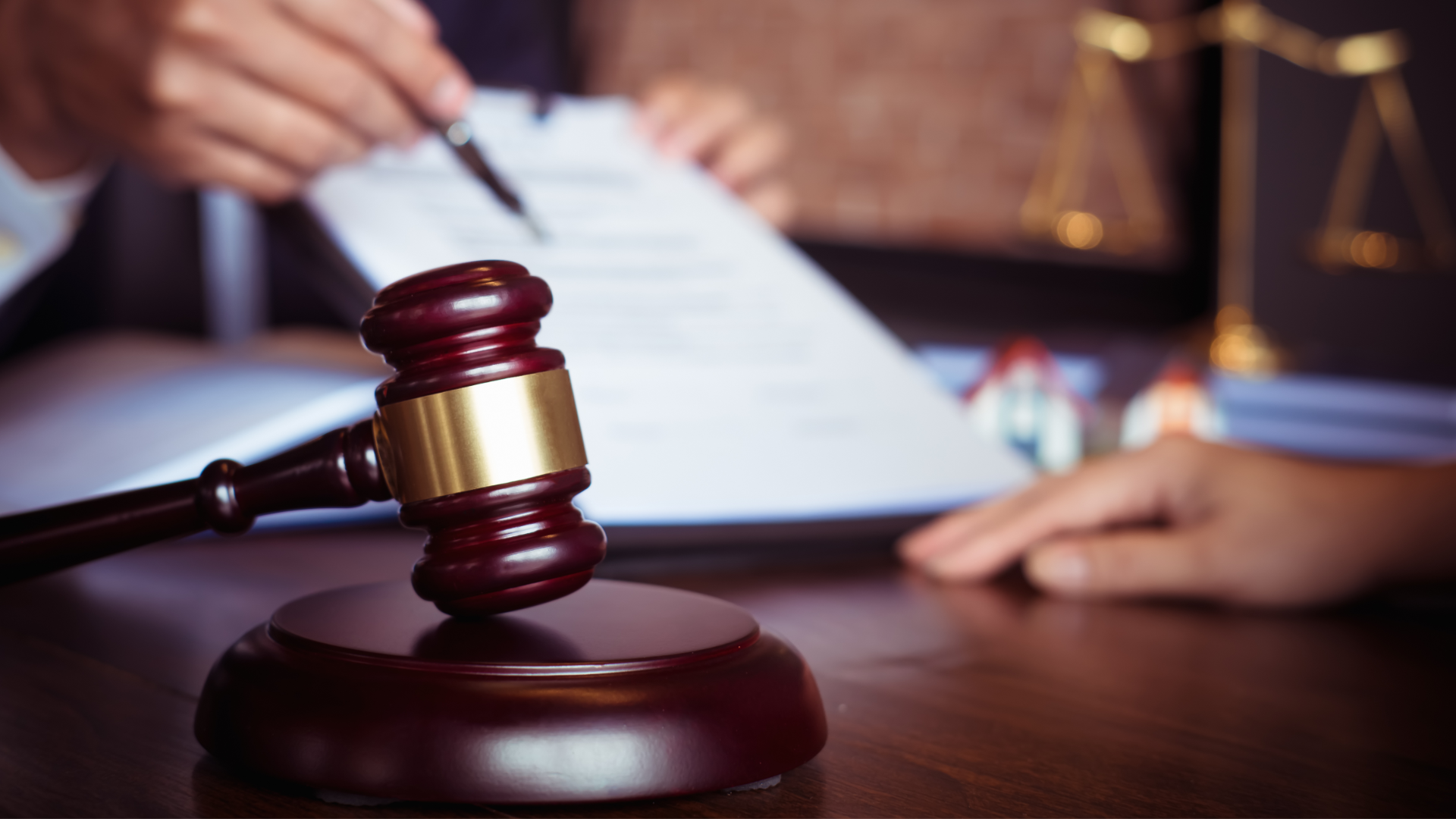 Two hands, one holding pen and paper, with a gavel in the foreground signifying a court order